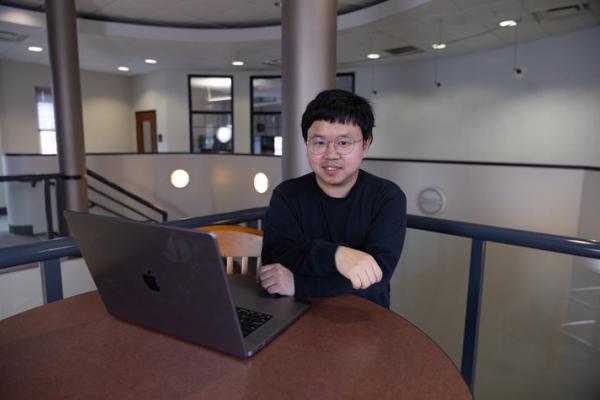 Xin Liang sitting at desk with laptop 
