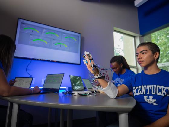 3 Students in front of a TV displaying images created from sensors that have been applied to a hand.