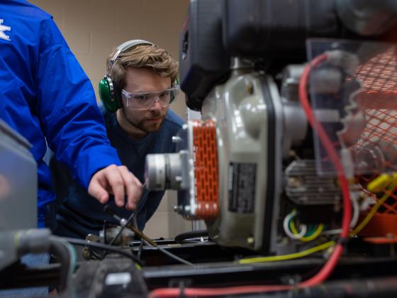 Student looking at an engine wearing safety glasses and headphones